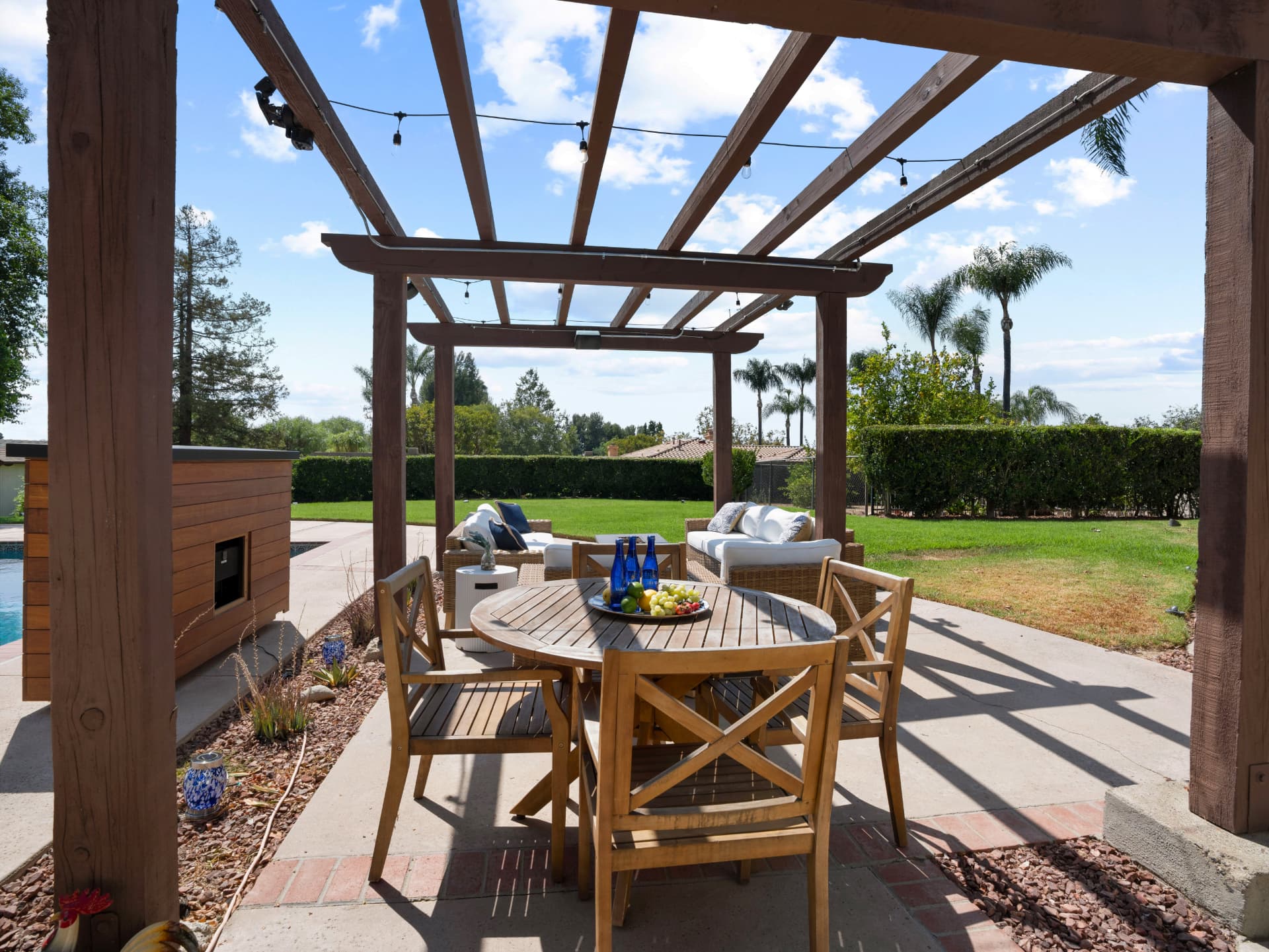 Covered pergola with outdoor dining table beside the lawn and pool
