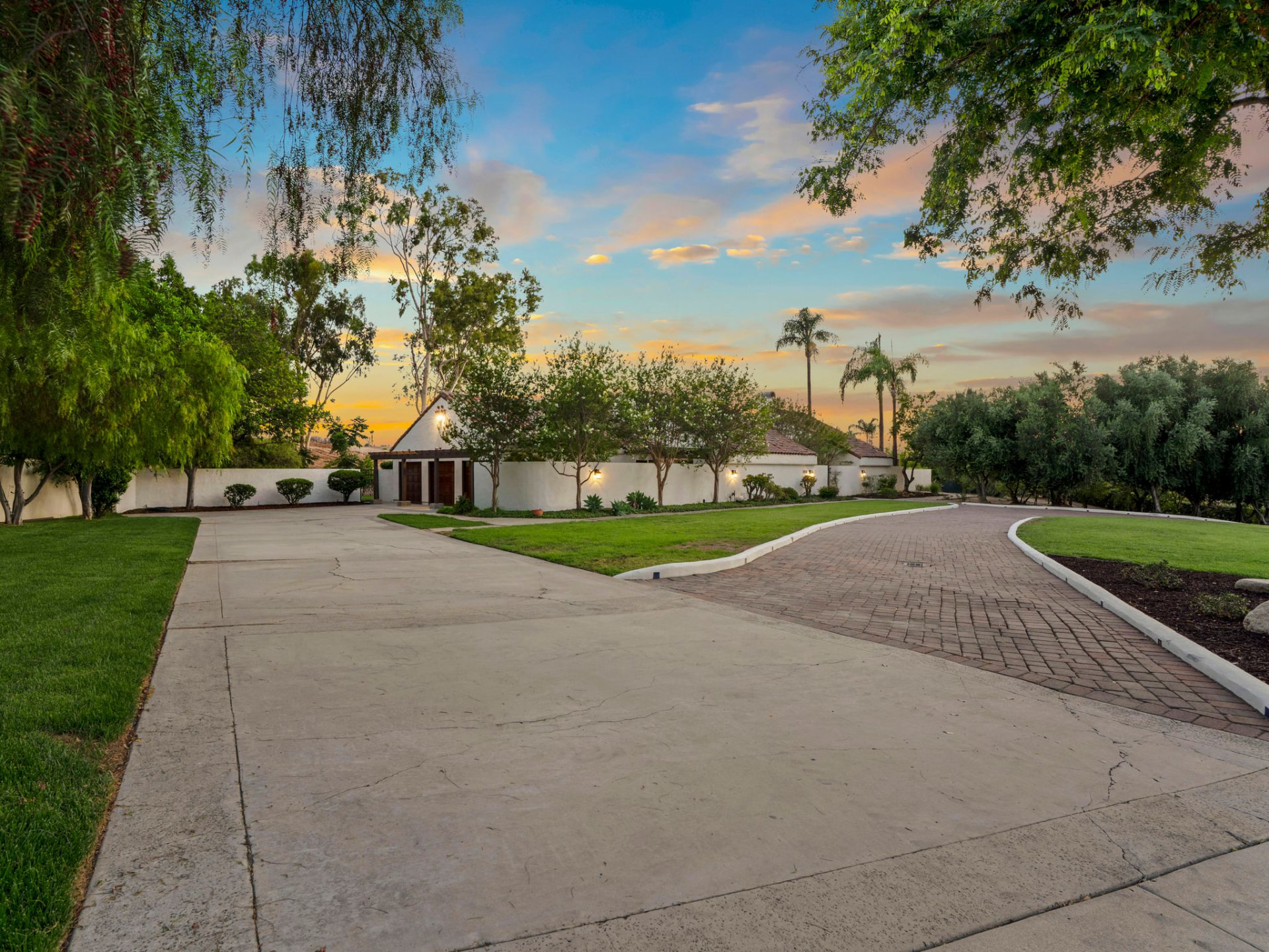Long private driveway at sunset leading to the walled front entry and mature landscaping