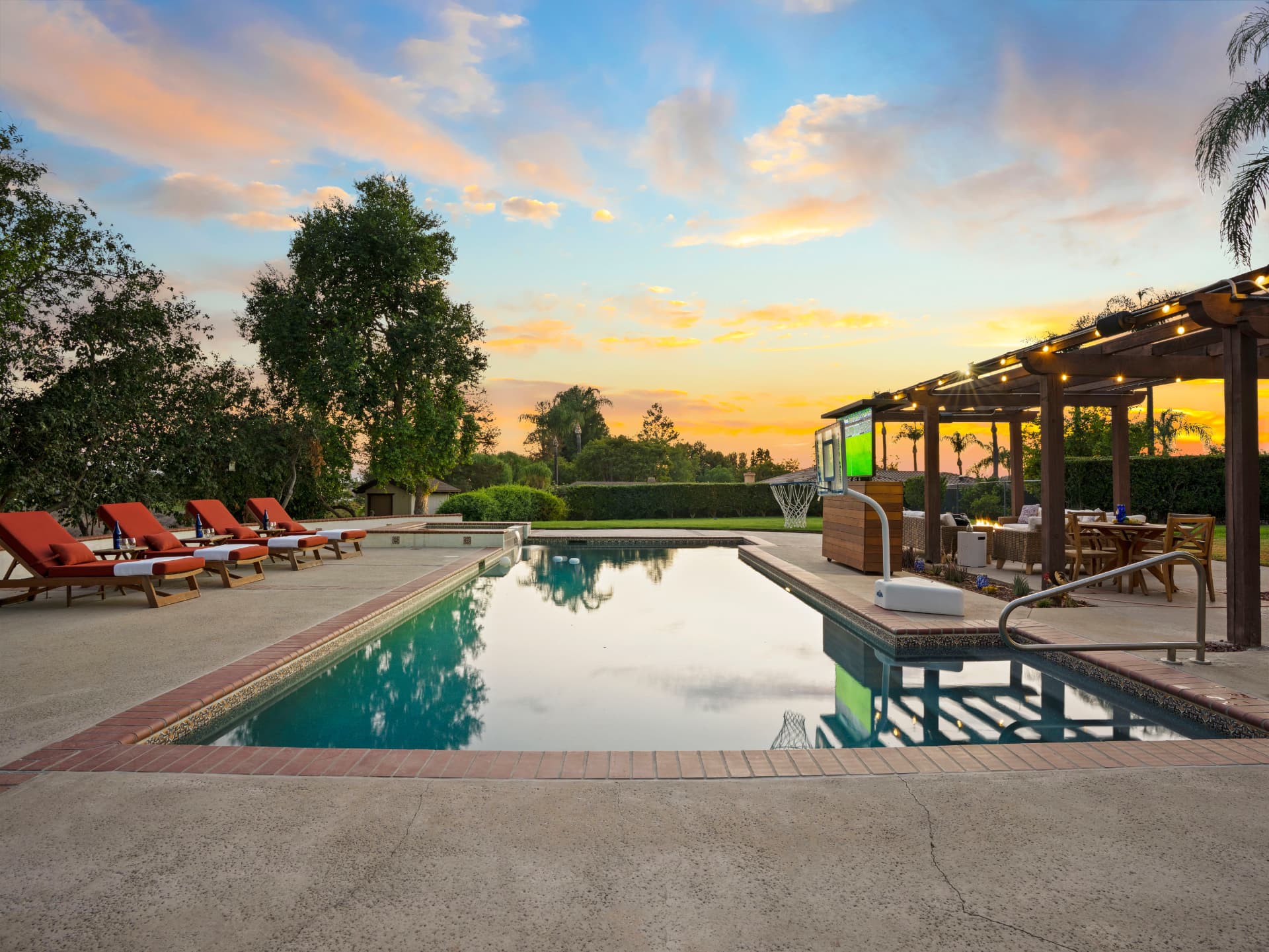 Rectangular pool at sunset with lounge chairs, pergola and string lights